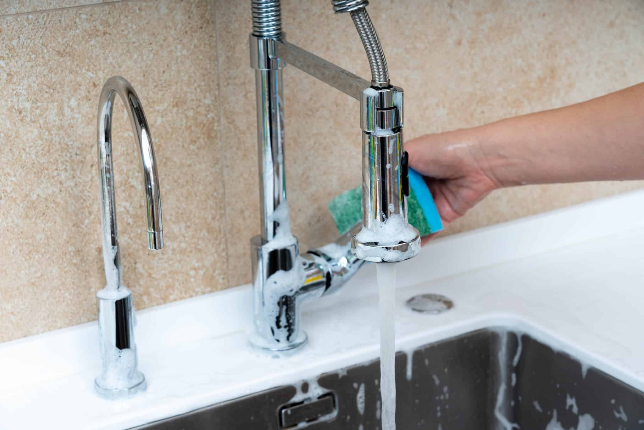 Cleaning a kitchen faucet and sink with a sponge and soapy water under running water, Faucet Installation Service.