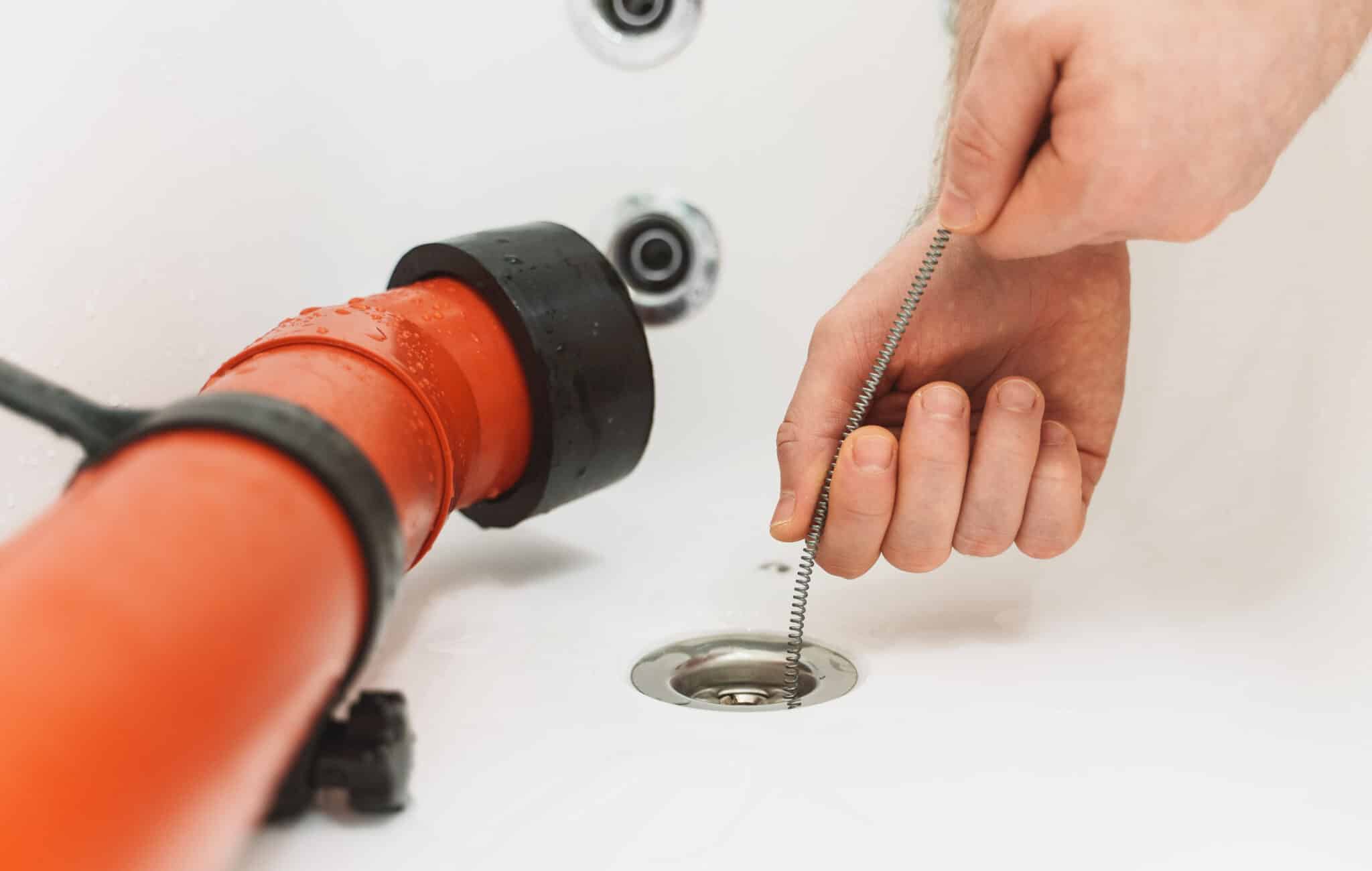 Plumber using drain snake to unclog bathtub., Clogged Drain Prevention.