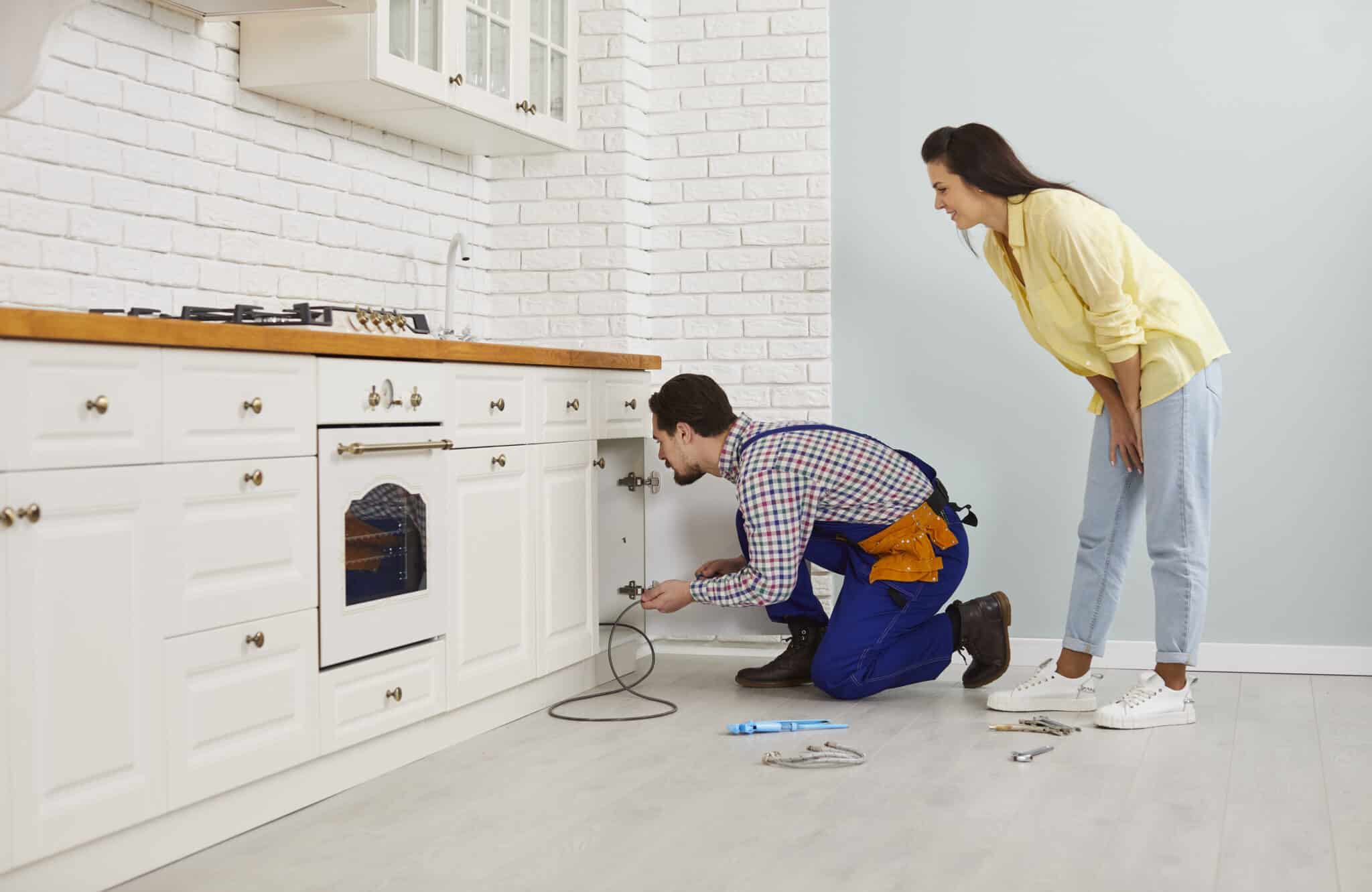 Young girl calls the plumber to fix the problem of a clogged drain under her kitchen sink, Clogged Drain Prevention.