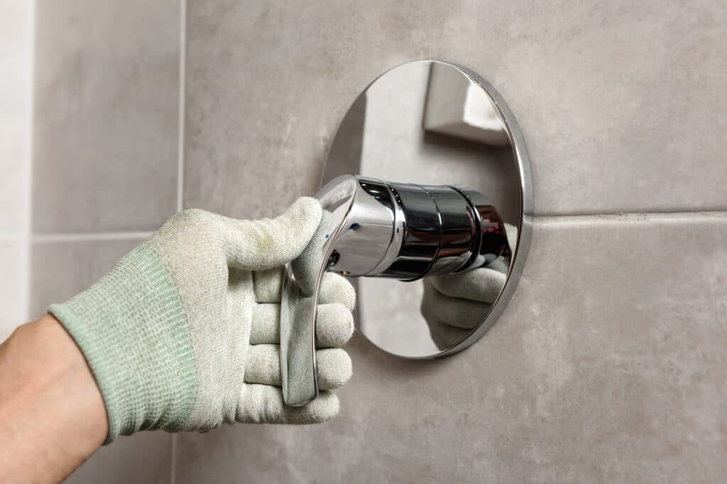 Plumber doing a shower valve replacement without tearing into tile, wearing protective gloves.