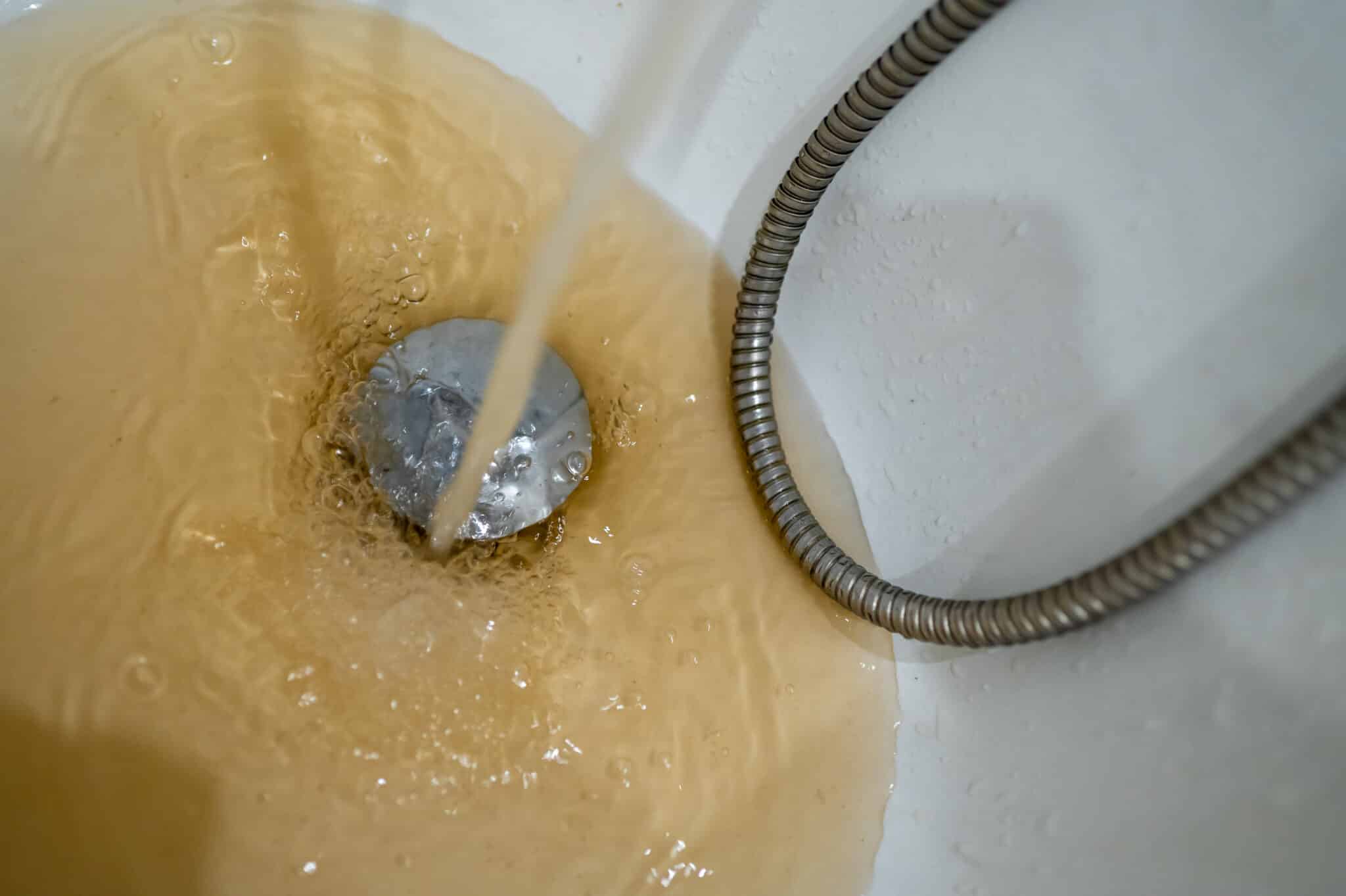 Pipe Descaling Restores Flow and Reduces Corrosion 1 Contaminated brown water running into a white bath drain, Pipe descaling.