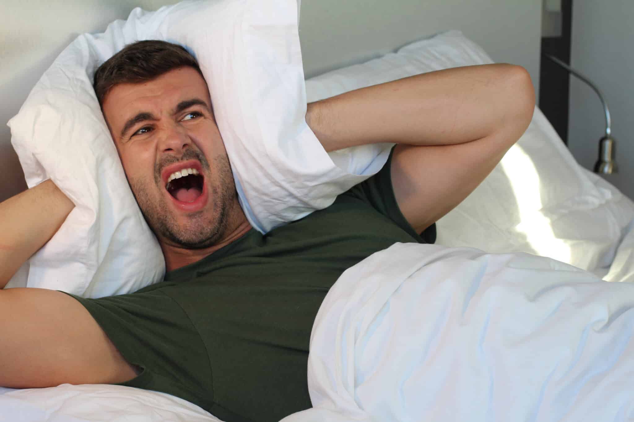 Air Conditioner Repair Troubleshooting for Faster Cooling 1 A frustrated man covering his ears with a pillow due to the noisy AC, likely needing air conditioner repair.